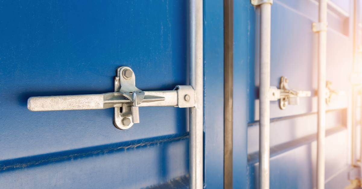 A close-up of a blue commercial cargo shipping container with a silver locking mechanism and a padlock.