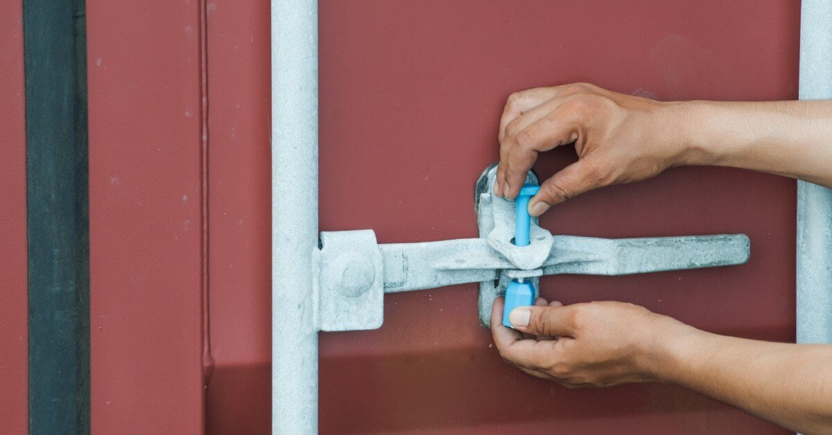 Close-up of a worker's hands securing a bolt security seal into the latch of a dark red shipping container.