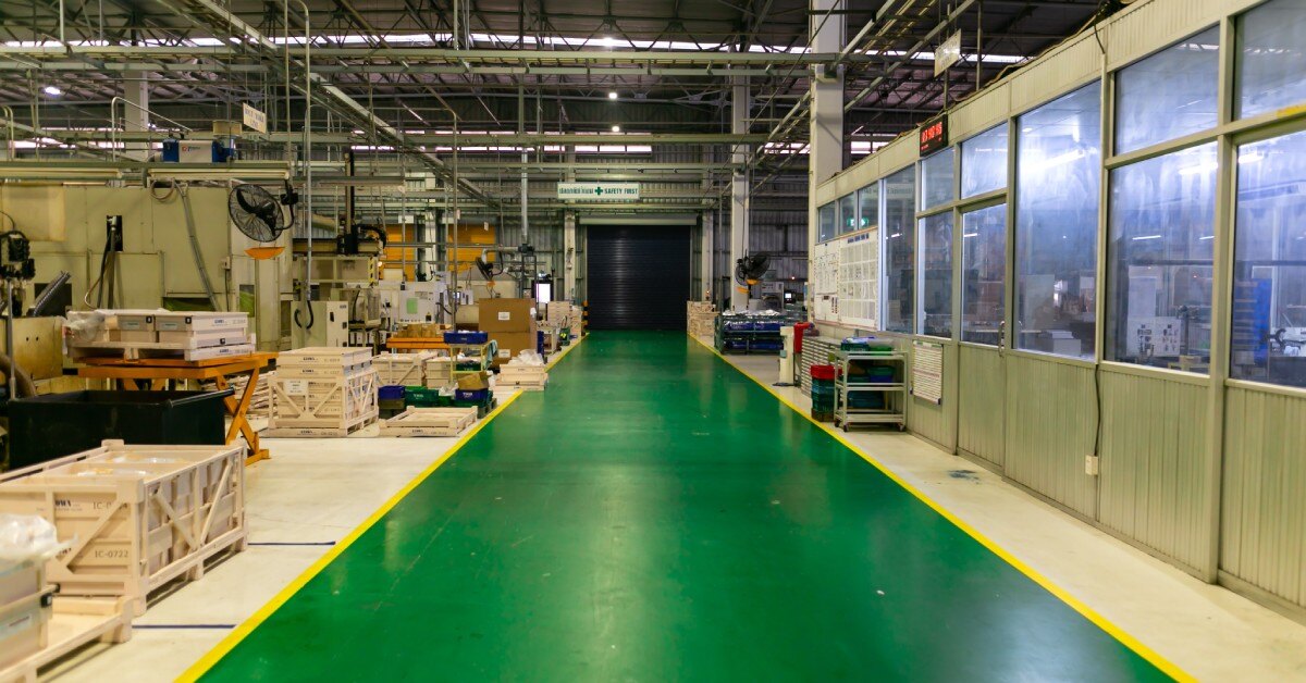 A warehouse with a barrier to the right, goods on the left, and a center walkway painted green on the floor and yellow outline.