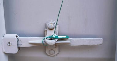 A green plastic seal attached to a latch, protecting a large gray container found in a warehouse from tampering.