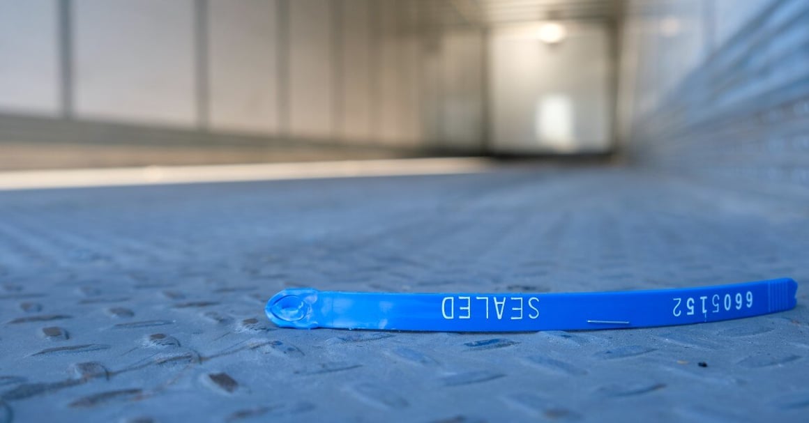 A broken blue plastic tamper-evident security seal on the ground, indicating something was tampered with.