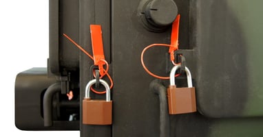 A close-up of two locks and two orange plastic tamper-evident security seals on a piece of equipment, preventing tampering.