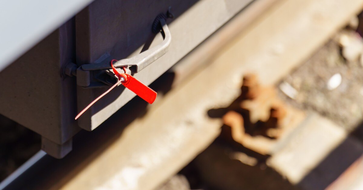 A small red plastic security seal is on the door handle for a container. The seal is intact and not broken.