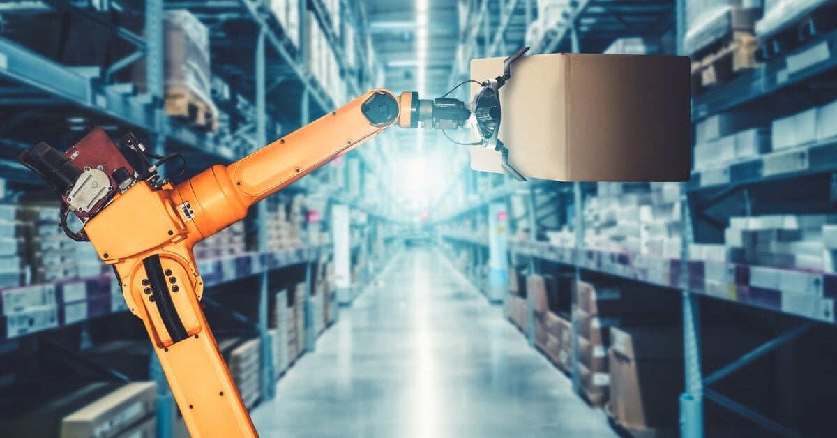 In the center of an aisle, an orange robot arm uses its prongs to pick up a box from a shelf in a warehouse filled with goods.