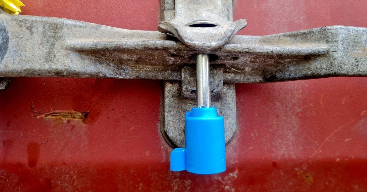 A close-up of a security padlock seal on the handle of a red container. The seal is locked, securing what is inside.